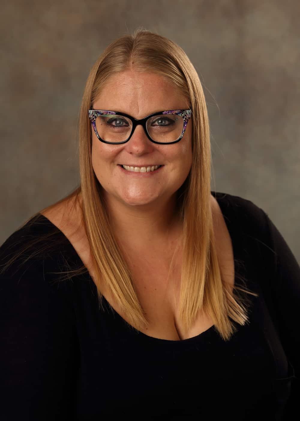 A photo of Executive Director Ashley Harms. She is a Caucasian woman with long blonde hair, blue eyes, and glasses with black and floral frames.