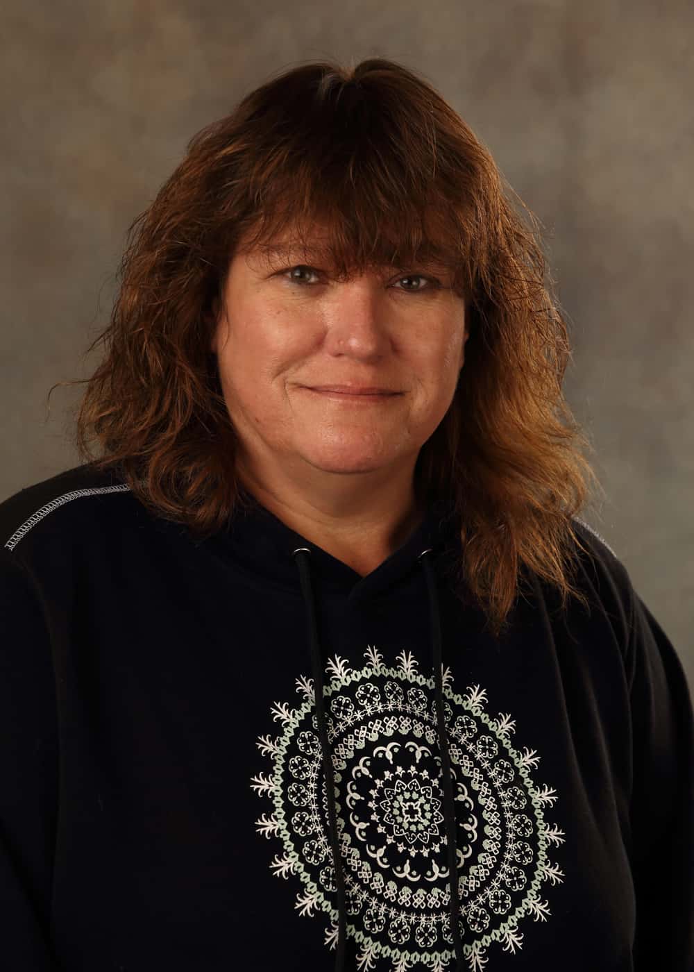Photo of Co-Teacher Debra Lampe. She is a Caucasian woman with long brown hair. She is smiling and wears a black sweatshirt with a white mandala-like design on it.