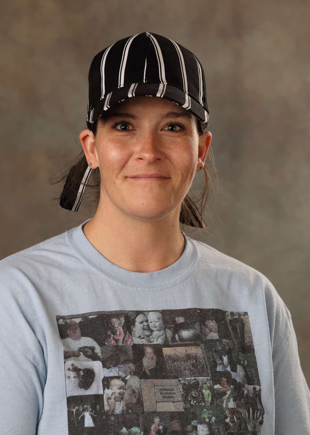 Photo of Kitchen Assistant Heat Riley. She is a Caucasian woman with brown hair and hazel eyes. She is smiling and wears a black and white striped hat and a light gray T-shirt with a collage of family photos on it.