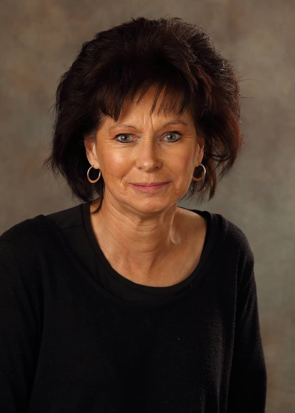 Photo of Co-Teacher Kathi Gemmell. She is a Caucasian woman with black hair and green eyes. She is wearing hoop earrings and a black shirt.