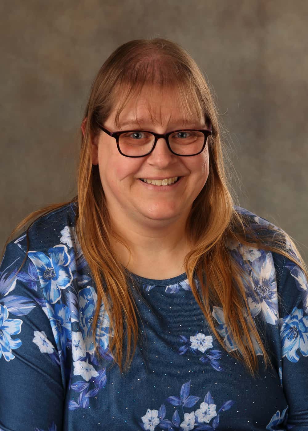 Photo of Lead Teacher Melissa Spaulding. She is a smiling Caucasian woman with long blonde hair, blue eyes, and black-framed glasses. She is wearing a blue shirt with a light blue and white floral pattern.